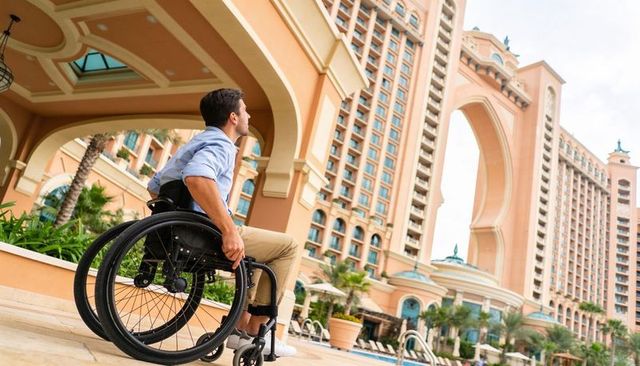 Man in wheelchair admiring luxury resort architecture and poolside palms at hotel entrance