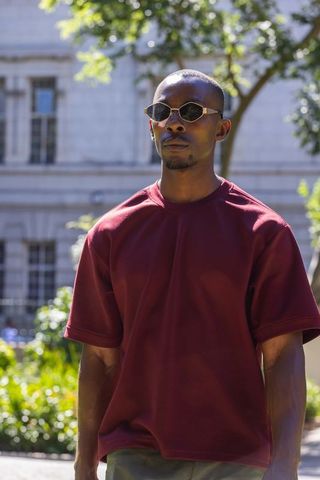 African american man wearing sunglasses and maroon shirt walking in sunlit urban plaza