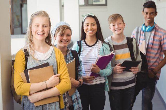 Group of smiling students standing with notebook in corridor at school