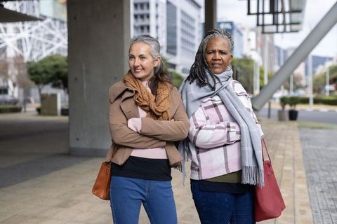 Mature women standing together smiling and looking confident in urban plaza with scarves