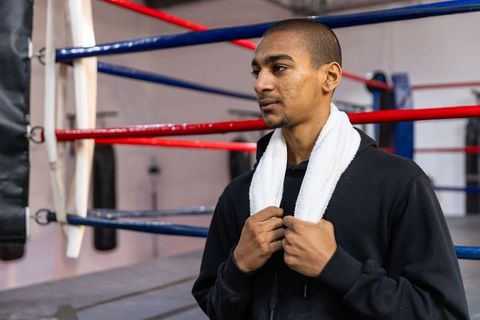 Young asian boxer standing in ring holding towel, focused athlete wearing hoodie