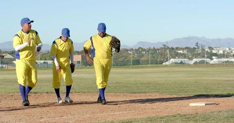 Three baseball teammates walking infield in yellow uniforms on sunny community field