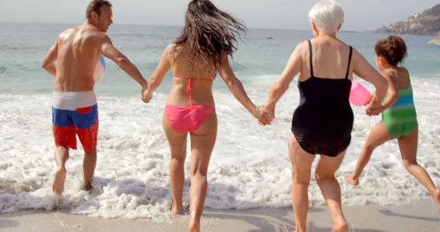 Happy and diverse family group holding hands and running into ocean waves from beach, showcasing a multigenerational bond and joyful moments during vacation. Suitable for use in travel promotions, family vacation ads, lifestyle blogs, or social media content celebrating family togetherness.