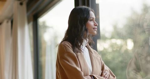 Young woman gazing out tall window in minimalist home contemplative lifestyle portrait