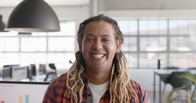 Portrait of happy biracial businessman with dreadlocks looking at camera and smiling at office. Business and work, unaltered.