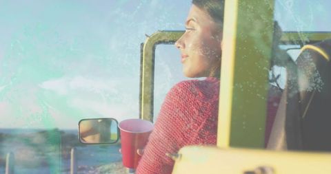 Woman gazing at ocean from yellow jeep holding red cup, sunlit seaside road trip