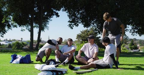 Young diverse men resting on park grass after sports training, laughing and bonding