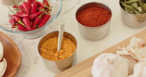 Stainless steel cups showcasing turmeric and paprika with garlic and red chili on marble