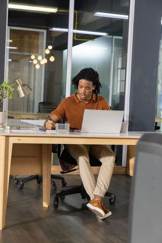 African american professional working at modern open-plan desk writing with laptop