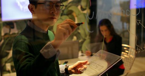 Focused Professional Writing on Transparent Board in Modern Office