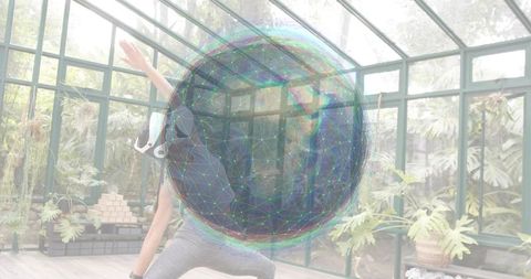 Woman stretching in glass greenhouse practicing yoga with holographic sphere