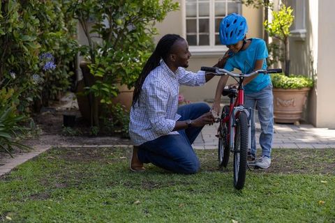 African american father teaching son to ride bicycle in suburban garden wearing helmet