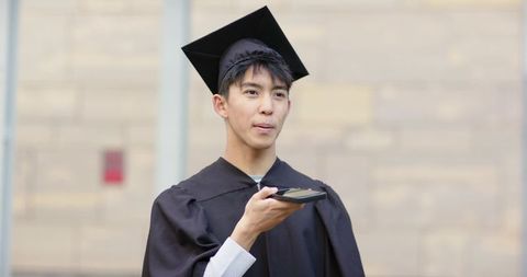 Asian graduate speaking on smartphone for virtual celebration or remote interview