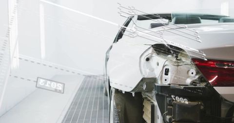 White sedan rear quarter panel removed in paint booth showing exposed frame and taillight