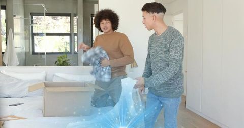 Roommates sorting clothes during move-in in sunlit minimalist bedroom with cardboard box