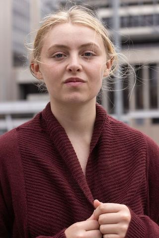 Young woman standing on rooftop holding burgundy knit sweater with wind-lifted hair