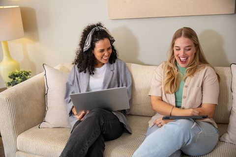 Diverse Friends Laughing Together with Devices on Sofa