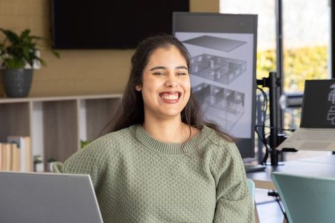 Smiling asian woman working on architectural floor plans in modern design studio