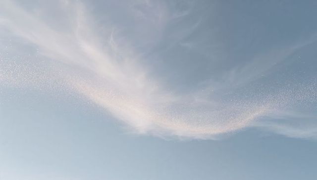 Ethereal wispy cirrus cloud with sparkling trail arcing across pastel blue sky minimalist