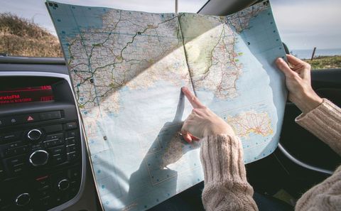 Pointing at coastal map inside car while planning scenic road trip route