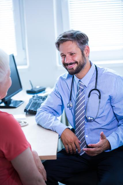 Doctor consulting with a senior patient in a medical office. The doctor is smiling and appears engaged in the conversation, creating a warm and professional atmosphere. This image can be used for healthcare websites, medical blogs, patient care brochures, and hospital promotional materials.