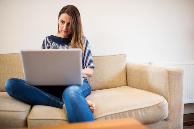 Woman sitting on sofa using laptop in living room - Download Free Stock Photos Pikwizard.com