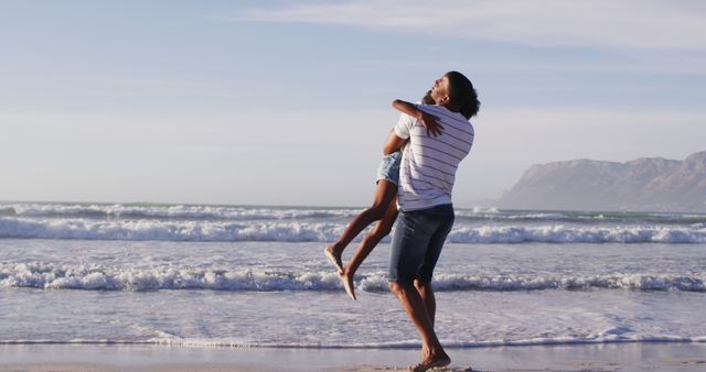Father spinning daughter on beach during sunny day. Person wearing casual summer outfit. Waves crashing in background. Perfect for souvenirs, family blogs, vacation promotions, and advertisements focusing on family bonding, summer holidays or beach destinations.