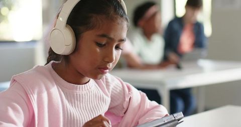 Asian student studying with headphones using tablet in bright classroom