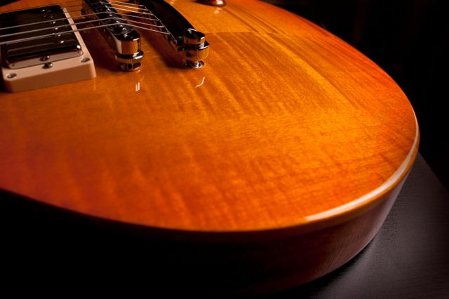 Close-up view of a polished wooden electric guitar body illuminated under warm, ambient lighting. The detailed wood grain and glossy finish are visible, highlighting the craftsmanship of the instrument. Useful for music articles, instrument craftsmanship showcases, and as a background image for digital media related to music and hobbies.