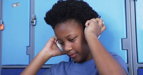 Teen student adjusting white headphones at blue school lockers listening to music