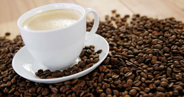 A white cup of coffee sits amidst a spread of roasted coffee beans on a wooden surface, with copy space. The scene evokes the rich aroma and warmth of freshly brewed coffee, inviting a moment of relaxation.