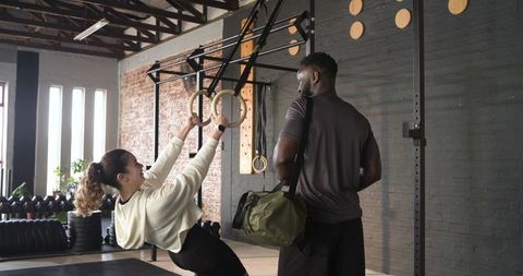 Personal trainer assisting client with ring rows in industrial gym setting