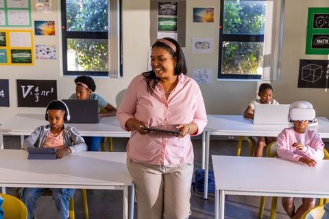 African american teacher leading diverse students with tablets, laptops and vr in classroom