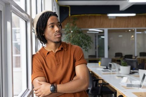 Thoughtful african american man leaning by window and looking in modern coworking workspace
