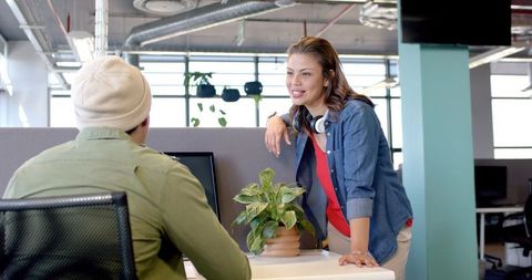 Young Colleagues Leaning on Cubicle Partition Collaborating in Bright Open Office Workspace