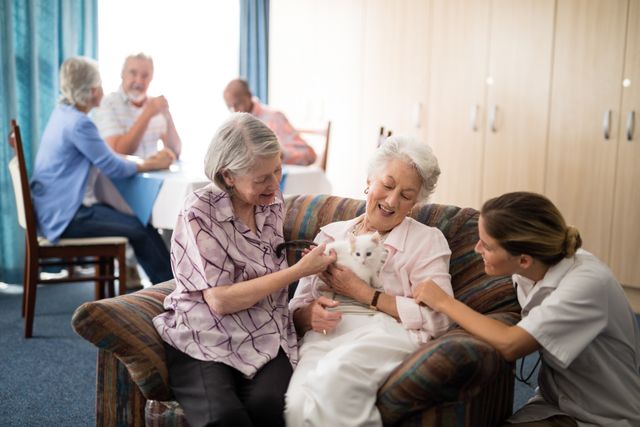 Seniors and a caregiver are enjoying time together with a kitten in a nursing home. This image can be used for promoting senior care facilities, highlighting the benefits of pet therapy, or illustrating the importance of companionship and social interaction in elderly care settings.