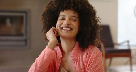 African american woman smiling leaning resting hand on face in pink jacket