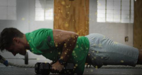 Man holding plank on hex dumbbells performing intense core workout near battle rope