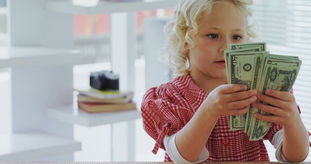 A young Caucasian girl examines a handful of dollar bills, with copy space. Her curious expression suggests she is learning about money or perhaps playing a game involving finance.