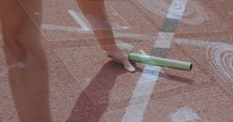 Close-up sprinter gripping green baton during relay exchange on sunlit running track