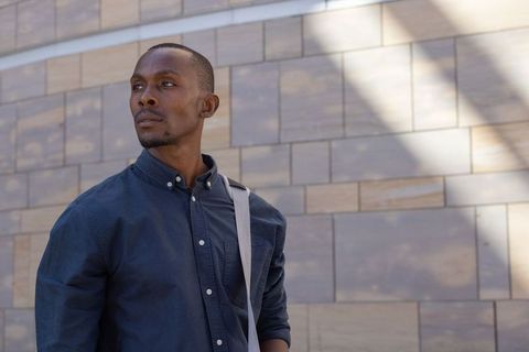 Urban professional looking confidently left against sunlit stone wall with shoulder bag