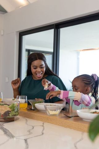 African american mother and daughter sharing meal and laughing at modern kitchen counter