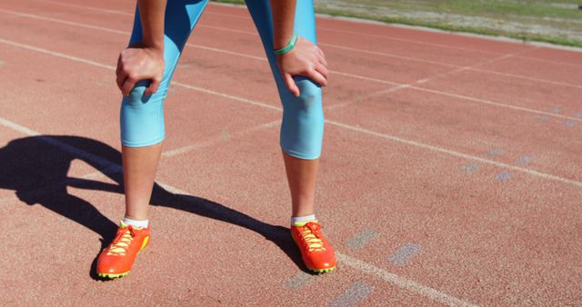 An athlete wearing bright orange running shoes and blue athletic wear takes a break on a running track. Ideal for use in health and fitness promotions, sportswear advertisements, or athletic training materials.