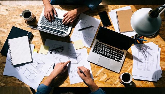 Designers collaborating on product sketches and laptops at busy studio desk