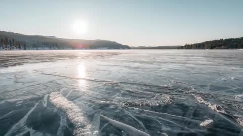 Drone gliding over frozen lake at sunrise revealing cracked ice and distant treeline