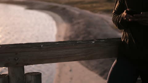 Man Using Smartphone Leisurely by Beach Promenade at Sunset