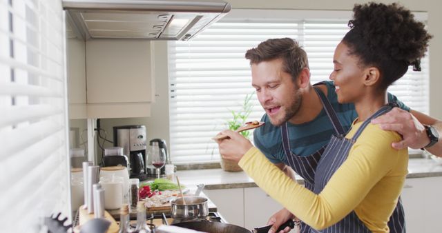 Image of happy diverse couple preparing meal, trying dish. Love, relationship and spending quality time together at home.