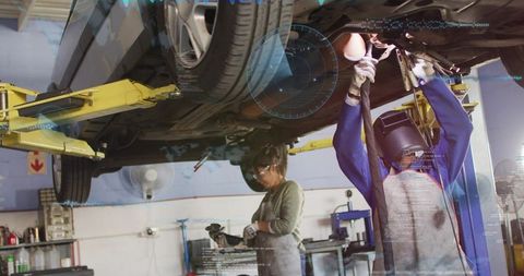 Female mechanics repairing car under lift with welding helmet teamwork in auto workshop