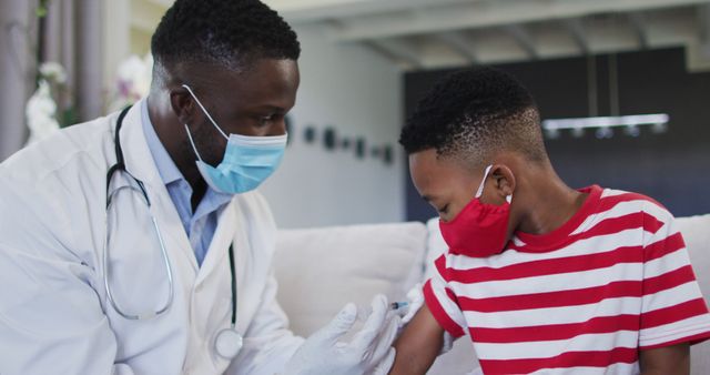 African american doctor wearing face mask injecting covid-19 vaccine into a boy at home. vaccination for prevention of coronavirus outbreak concept