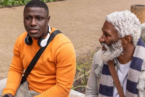 Intergenerational african american men talking on park bench wearing casual fall clothes